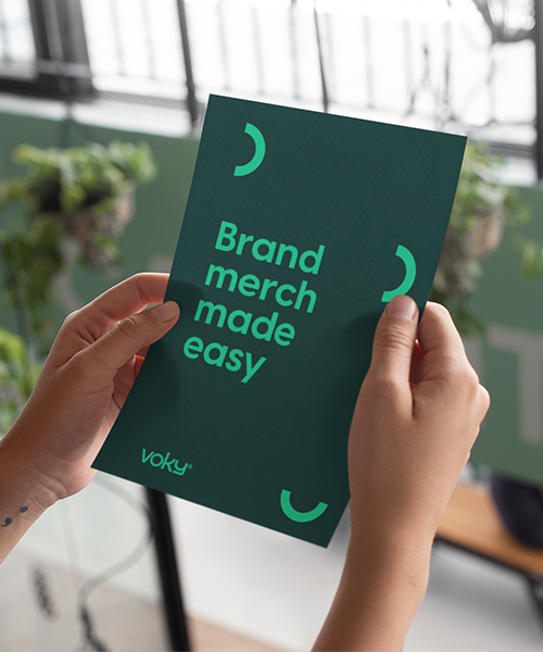Två händer håller i Voky-papper med texten ”Brand merch made easy”